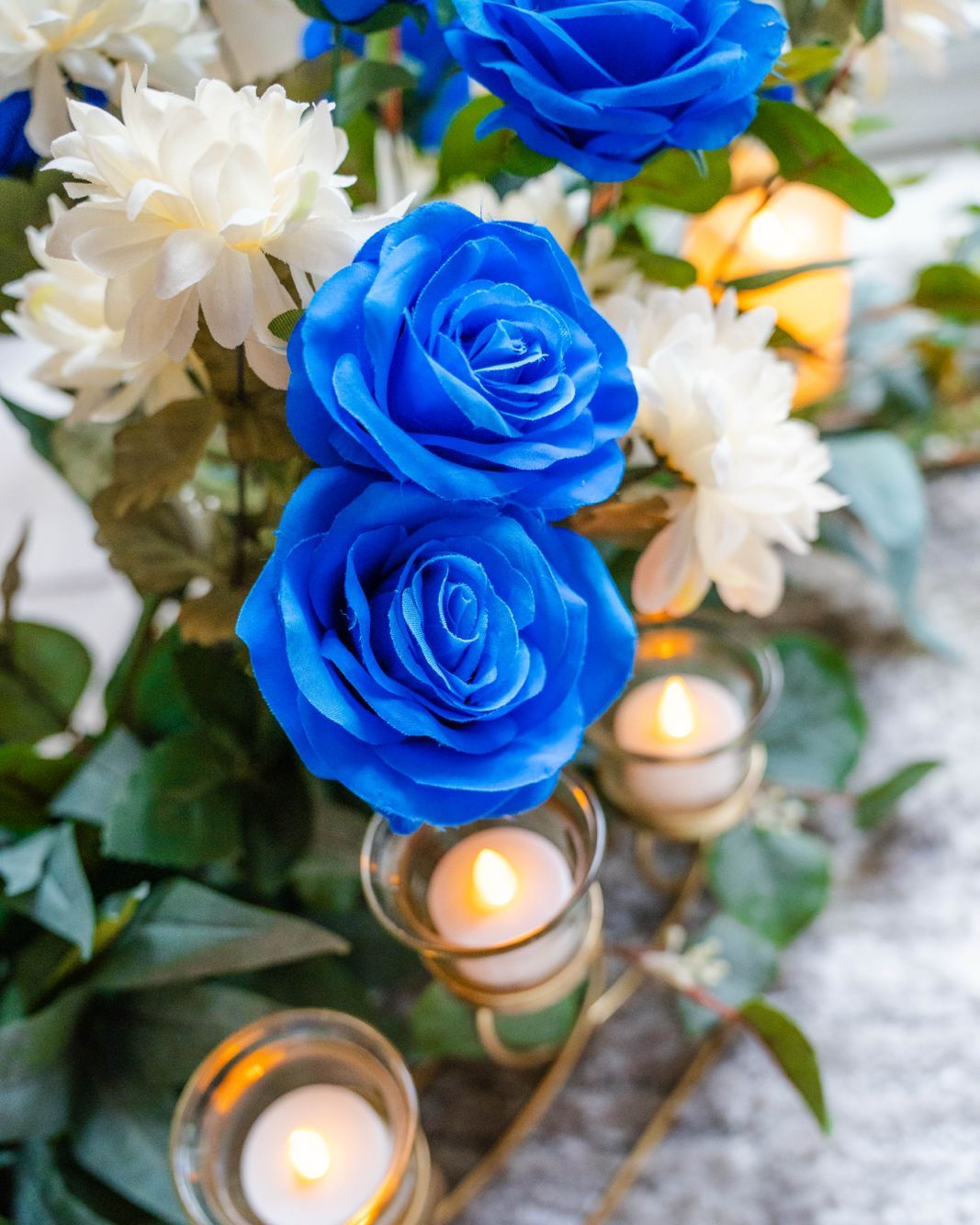 Close-up of blue roses, white blooms and candlelight in a Semai Events Decor arrangement
