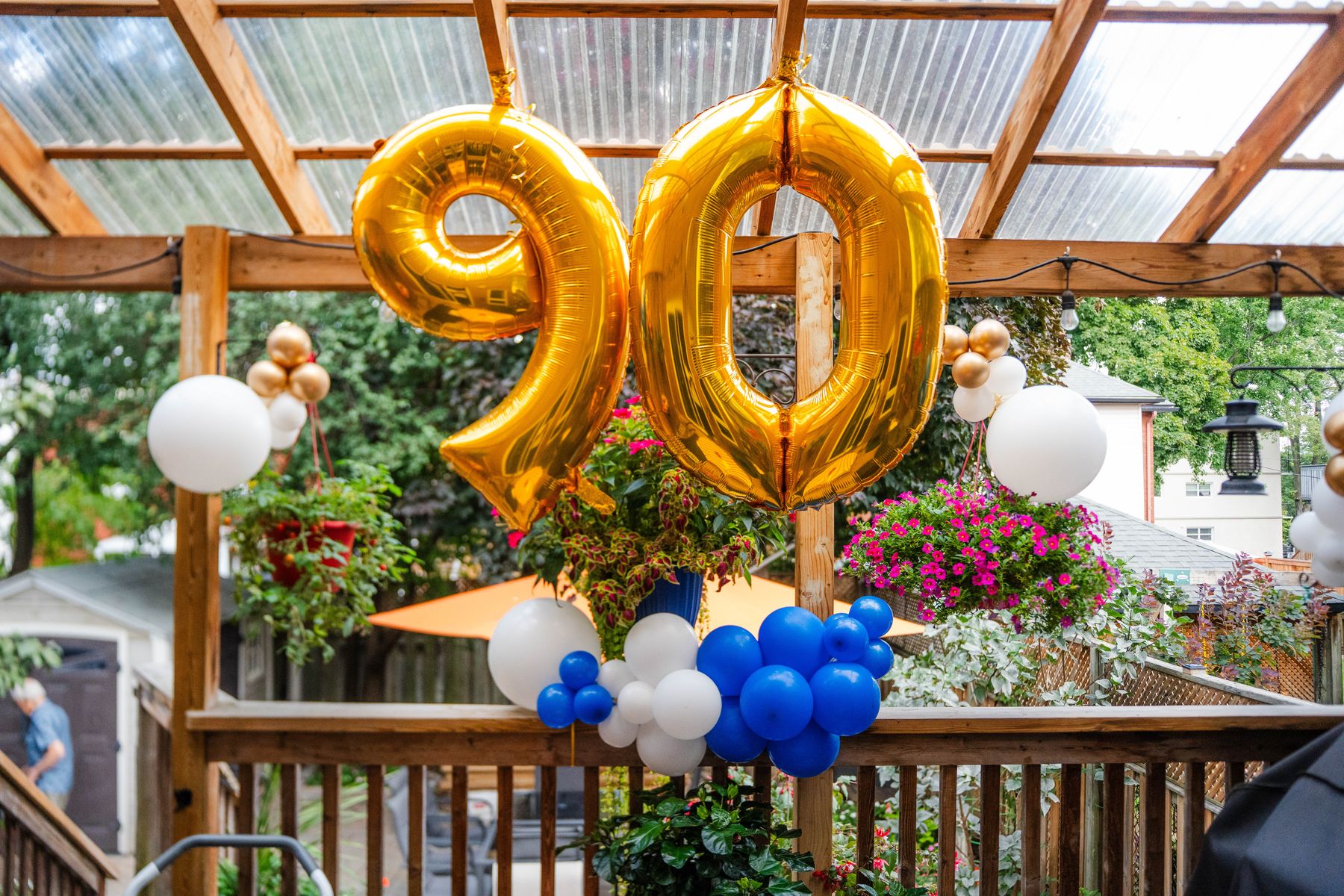 Ninetieth birthday decor with gold number balloons and a blue and white garland under a garden pergola