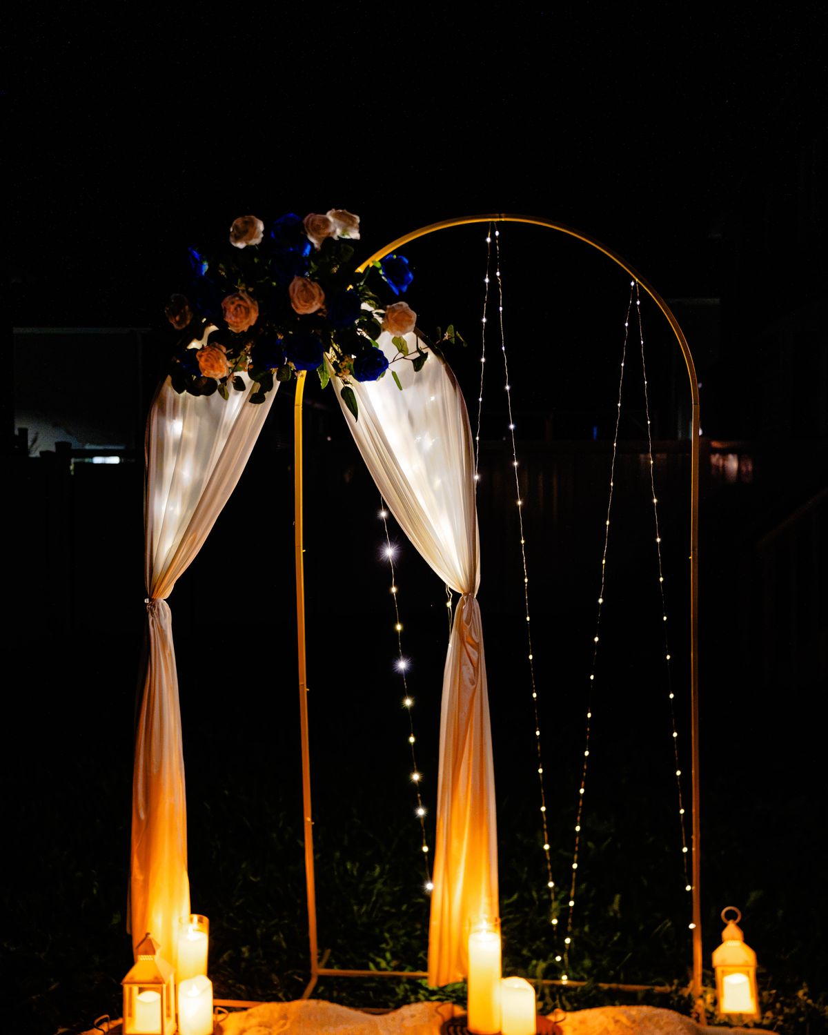 Candlelit gold arch with fairy lights and blue and peach roses at night
